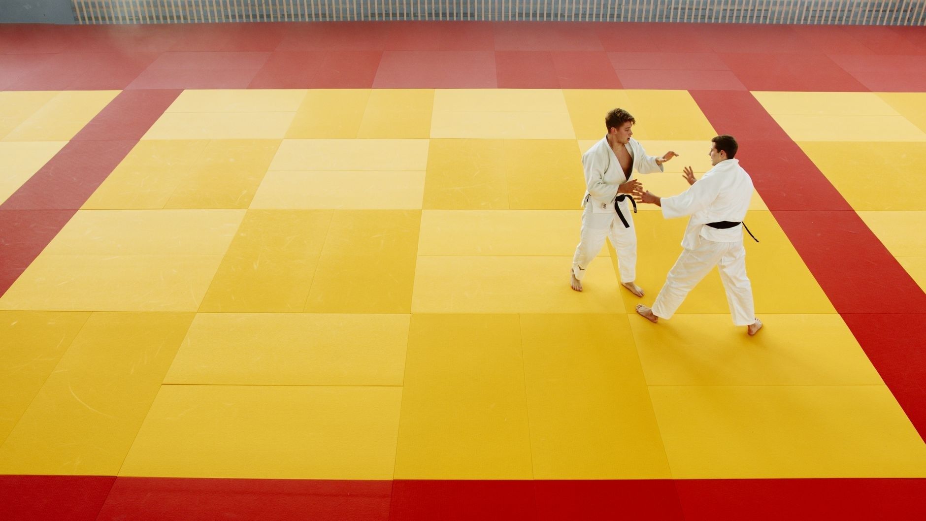 Zwei Judoka üben auf einer gelb-roten Matte eine Grifftechnik